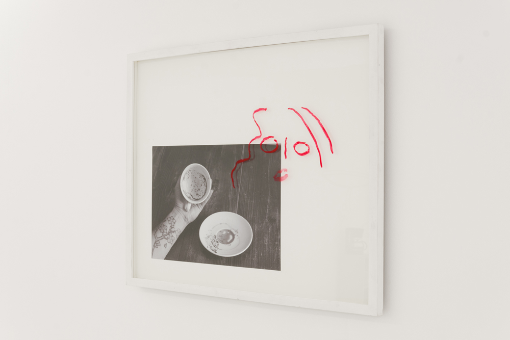 Framed black and white photograph of a hand holding a teacup with grinds in it and a lipstick drawing of a face on the glass 