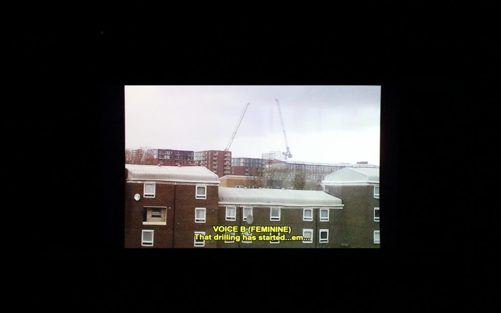 screening of Clare Charnley & Lucy Clout's 'The Fact That I Taught You to Speak − What's That?' showing various buildings with the caption 'VOICE B (FEMININE) That drilling has started...erm...'