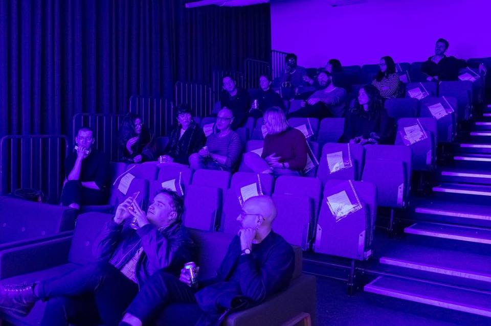 Audience on retractable seating bathed in a purple glow