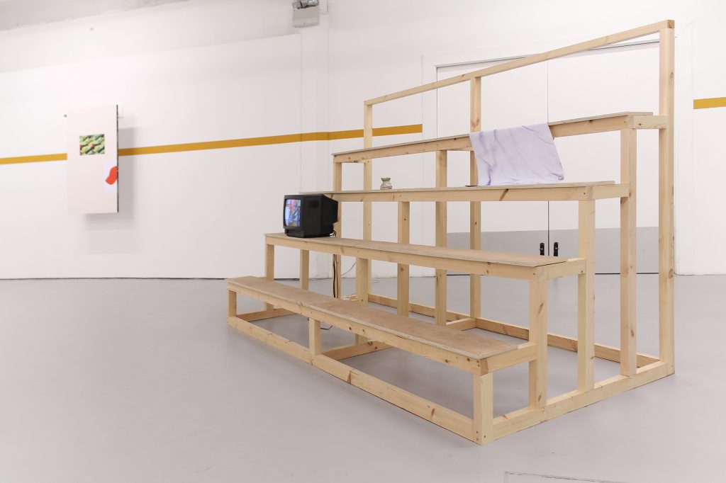 Wooden bleachers with a Television, an oil burner and a plastic banner draped on them.