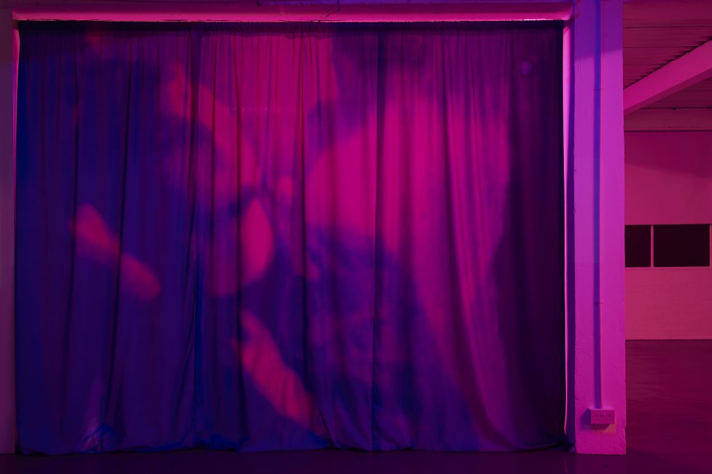 Pink image of large curtain with purple image of a dancing man leaning back hand on chest