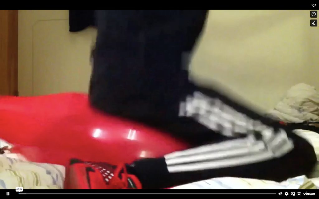 Screengrab of legs in black adidas three stripe joggers sitting on a red balloon.