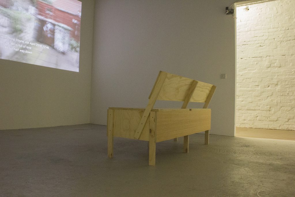 Wooden bench in a white space facing a projection of the video vaseline