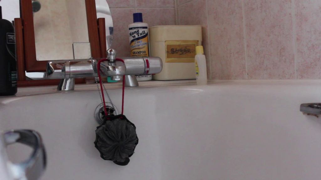 the corer of a bathtub with a bottle of Mane'n Tail shampoo and a plastic container with a crossed out label saying SUGAR