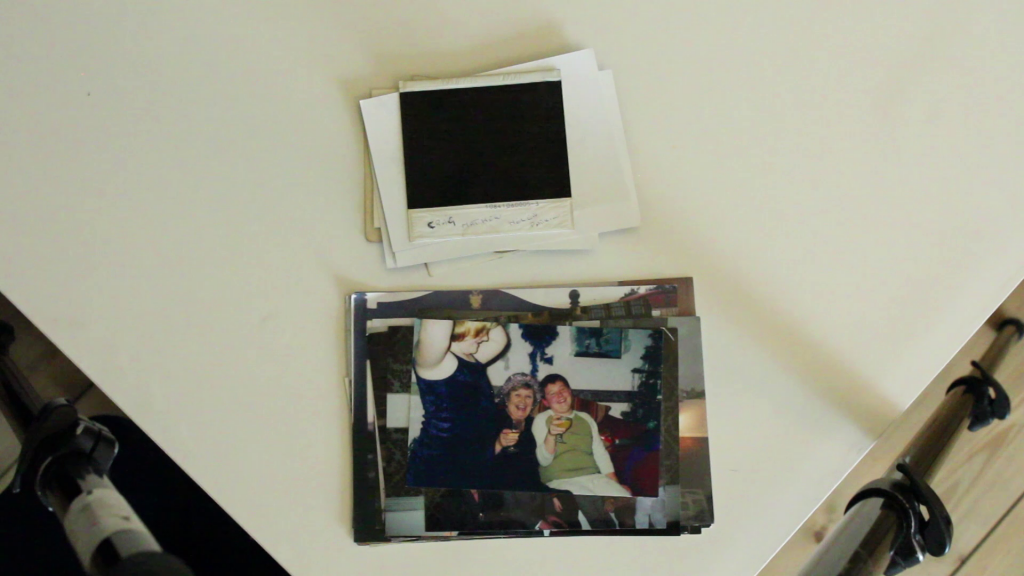 two piles of photos, face up and face down, on a white table, top image shows two people raising glasses