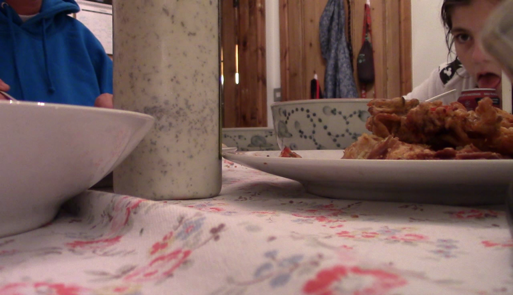 shot taken from table of bowls, garlic yogurt, onion bhajis, and a child licking the top of a can