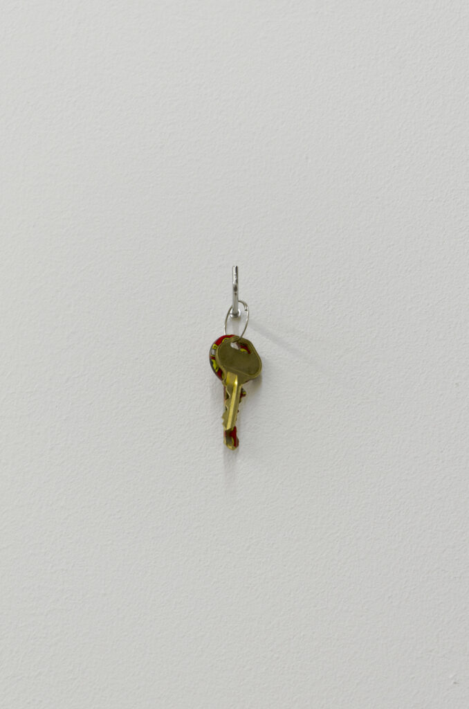 two keys, one plain one with a yellow and red pattern, on a hook on a white gallery 