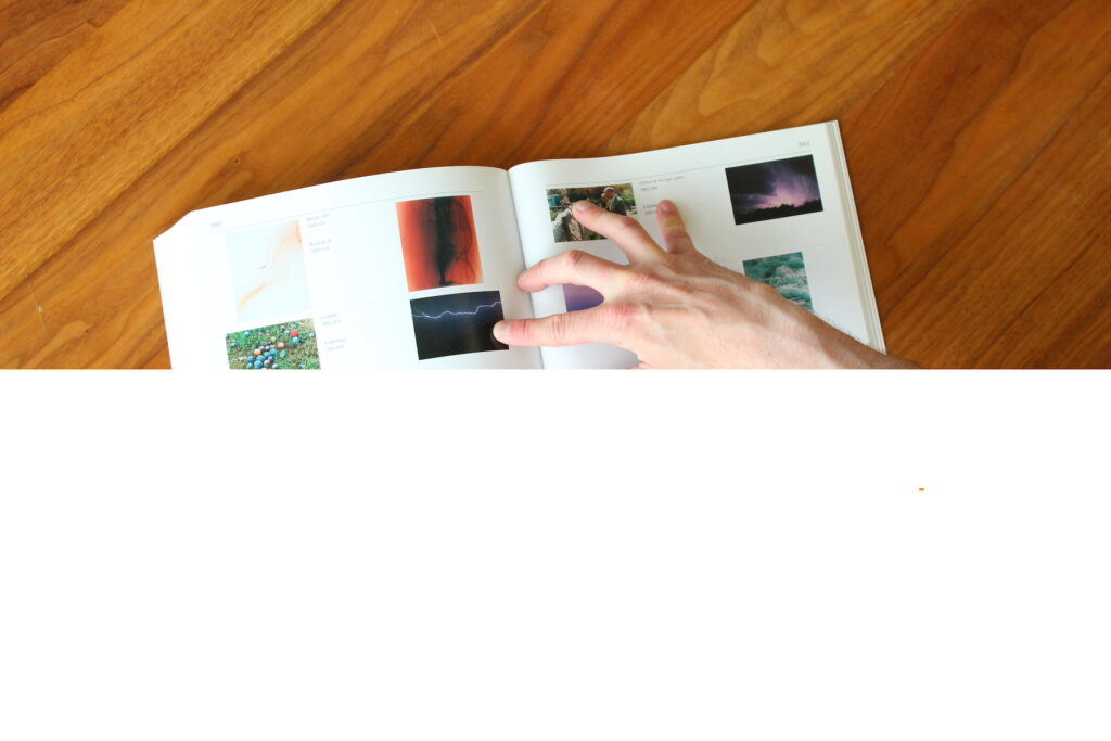 glitching image of hand holding open a Félix González-Torres book on a glossy wooden table, the photograph is half obscured by the glitch 