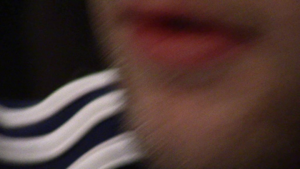 Blurry still of a pink mouth and white chin with blonde stubble take up two thirds of the right of the image, with three adidas whites stripes on the bottom left.