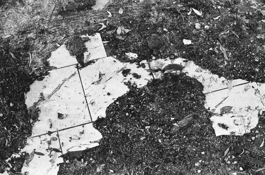 Black and white 35mm photograph of a rough wasteland floor with the half smashed remains of a previous tiled floor.