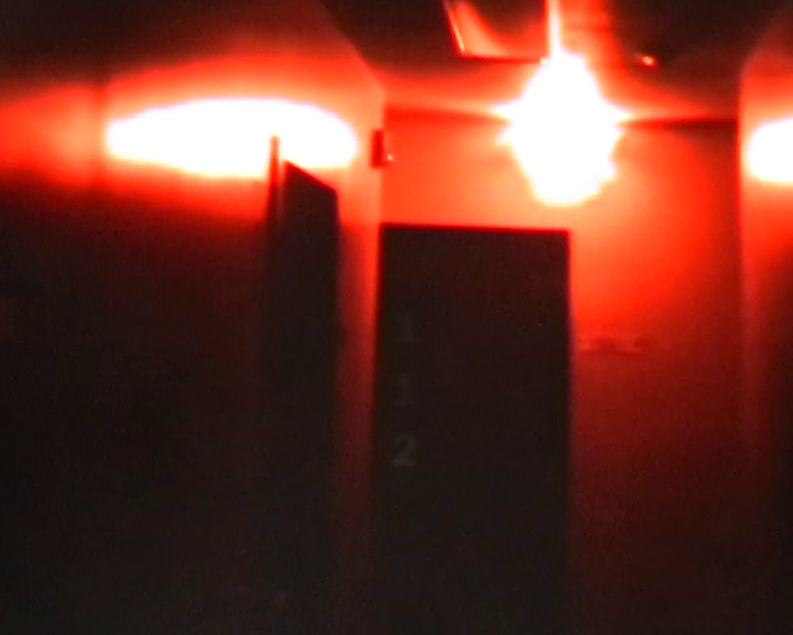 Dimly lit red hallway with a central door and bright overhead light.